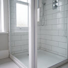 Corner of a white-framed shower enclosure with a white tray and metro tiles, seen through the glass door
