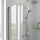 Vertical channel between two water-speckled glass shower panels, chrome riser rail and glass shelf behind
