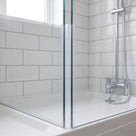 Clear corner seal down the vertical joint where two glass panels meet above a white tray, metro tiles behind