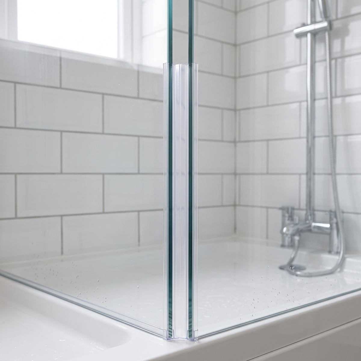 Clear corner seal down the vertical joint where two glass panels meet above a white tray, metro tiles behind