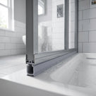 Grey seal under the rail of a grey-framed screen over a white bath, droplets on the glass, white metro tiles behind