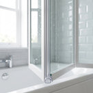 Clear seal at the foot of a folding bath screen upright, wet glass and metro tiles behind