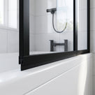 Black seal along the bottom rail of a black-framed bath screen above a white bath, black taps behind