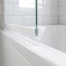 Clear seal on a bath screen's white bottom rail, blade angling down onto a wet white bath, metro tiles behind