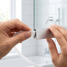 Hands sliding a white 5mm T-head shower seal into the open end of an aluminium bottom rail channel