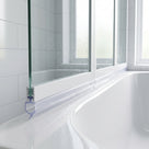 Clear seal with a small hooked cup blade under a white bath screen rail, on a curved white bath