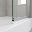White seal blade under the brushed aluminium bottom rail of a glass bath screen, resting on the white bath rim