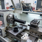 Black acetal rod clamped in the chuck of a lathe with a freshly turned black acetal bush and swarf in the tray below