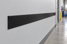 Illustrative 50 x 3mm black PVC flat bar installed as an industrial wall bump strip