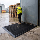 Black brush insert entrance matting, standard grid, surface-laid with ramped edging outside a warehouse personnel door, worker wiping site boots