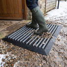Black brush insert entrance matting, wide grid, on the gravel threshold of a farm shop in winter, stones and slush falling through the wide grid under wellington boots