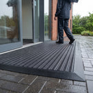 Dark grey brush insert entrance matting, standard grid, laid with ramped edging outside a glazed office entrance in the rain
