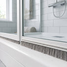 6mm x 12mm brush seal fitted along the bottom rail of a bifold shower door, grey bristles closing the gap to the tray