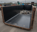Black HDPE lining panels fitted inside a rusty steel skip holding scrap, yard and plant behind
