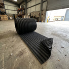 Roll of carpet insert entrance matting partly unrolled on a warehouse floor showing the scraper bars, carpet strips and open grid underside