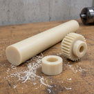 Cream cast nylon 6 rod on a timber bench beside a machined nylon spur gear and bearing bush, nylon swarf around them