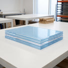 Stack of four acrylic sheets in pale blue protective film on a white bench, workshop tables and racking behind