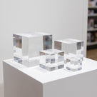 Four clear cast acrylic cubes in graduated sizes standing on a white display plinth, light catching their polished edges
