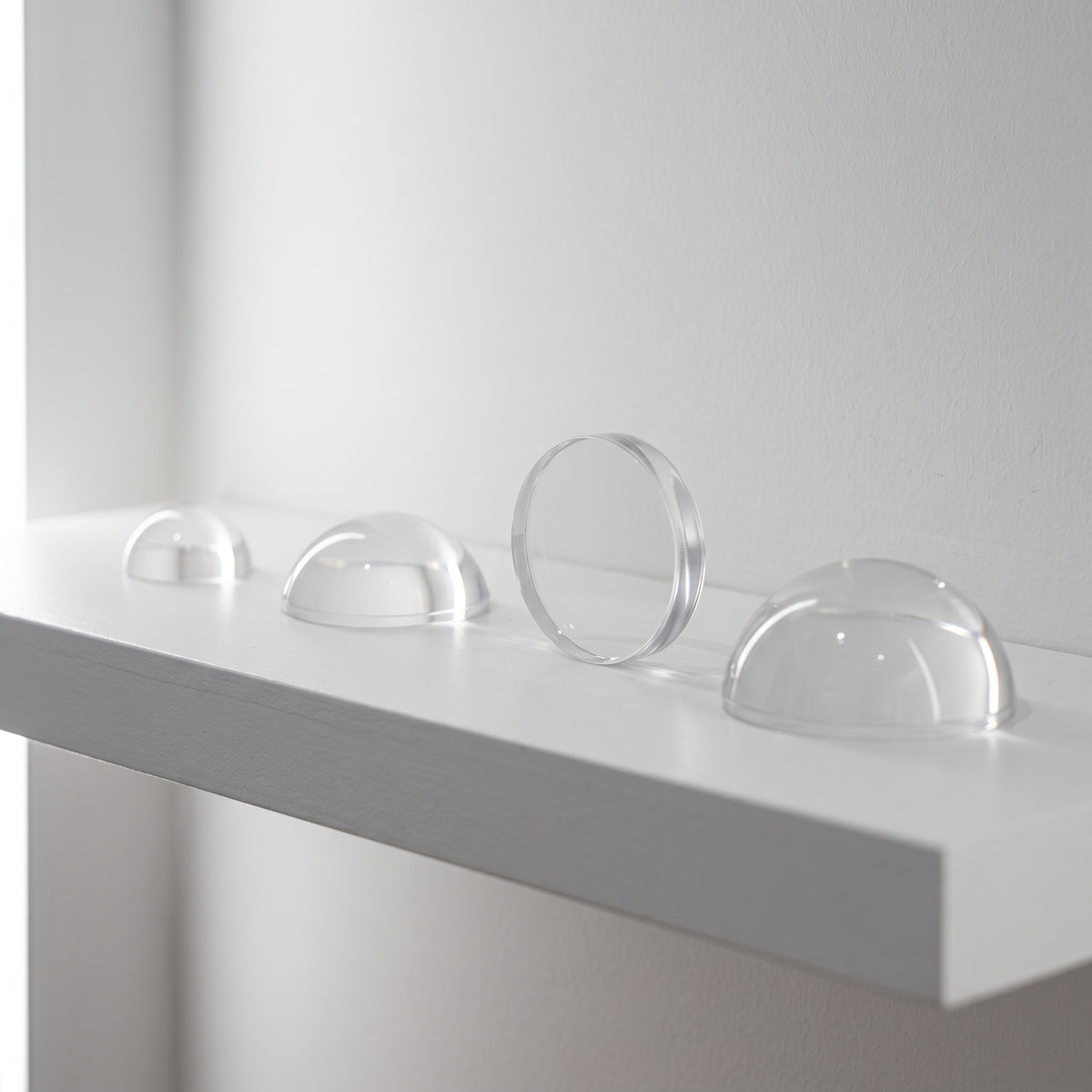 Three clear acrylic half domes on a white shelf with a flat disc stood on edge between them