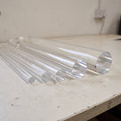 Clear acrylic rods of several diameters fanned across a scuffed white bench, round ends towards the lens