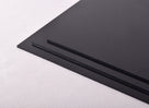 Two black polypropylene sheets stacked at an angle on pale textured fabric, sawn edges facing out