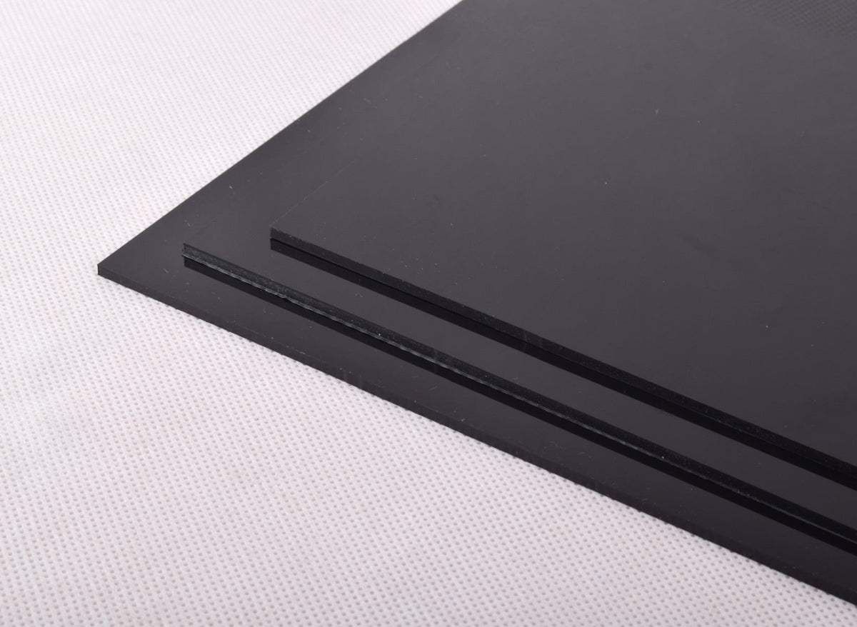Two black polypropylene sheets stacked at an angle on pale textured fabric, sawn edges facing out