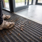 Close-up of muddy trainers on a ribbed entrance mat at a school doorway showing dirt and water trapped in the grooves