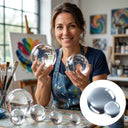Artist in a paint-spattered apron holding two clear acrylic spheres in her studio; inset shows two plain spheres.