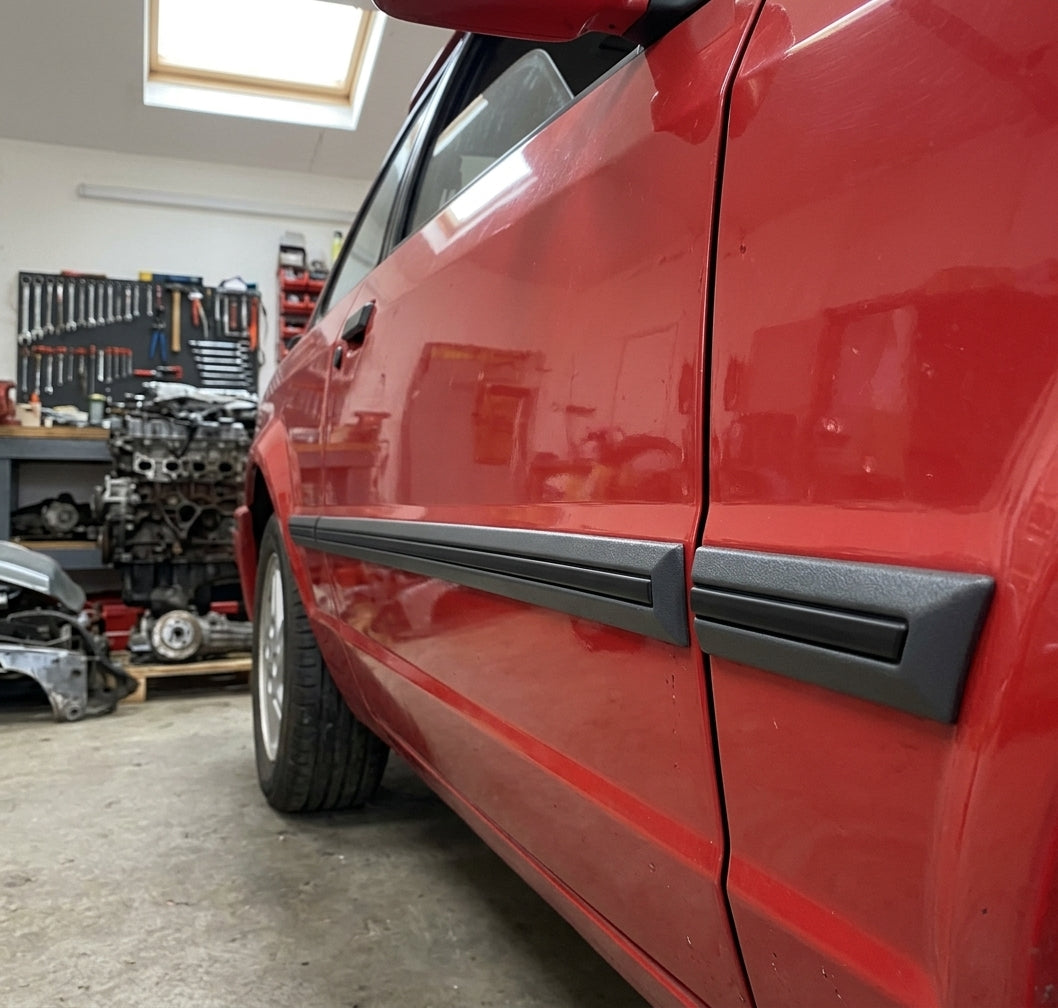 Black door mouldings fitted to a red car door, workshop with engine on stand
