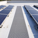 Grey embedded walkway matting set flush into a white liquid-coated flat roof as a straight maintenance path between rows of solar panels