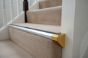 Bright gold anodised aluminium stair nosing end cap fitted to a carpeted staircase edge in a UK home hallway
