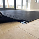 Black PVC joining strip under the seam between two lengths of black entrance matting, one edge lifted to show the strip