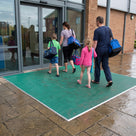 Holly green fine-ribbed open-grid entrance matting on paving outside a leisure centre, family walking in with swimming bags