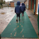 Holly green fine-ribbed open-grid entrance matting at a primary school entrance, children in wellingtons walking in from a muddy playground