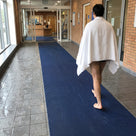 Oxford blue fine-ribbed open-grid entrance matting as a long run along a swimming pool entrance corridor, swimmer walking towards reception