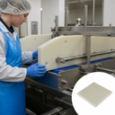 Worker in a blue apron fitting a thick cream nylon guide with bolt holes to a food conveyor