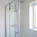 Clear seal down the upright of a glass shower door in a white tiled enclosure, window behind