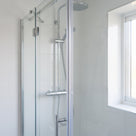 Clear seal down the upright of a glass shower door in a white tiled enclosure, window behind