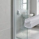 Cut length of the clear fin seal held large beside a glass shower door edge, grey tiled enclosure behind