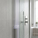 Clear fin seal down a glass shower panel upright against grey tiles, chrome valve and window behind