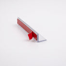 Clear L-shaped seal profile on white, red VHB tape strip on the upright with the liner tab peeled up