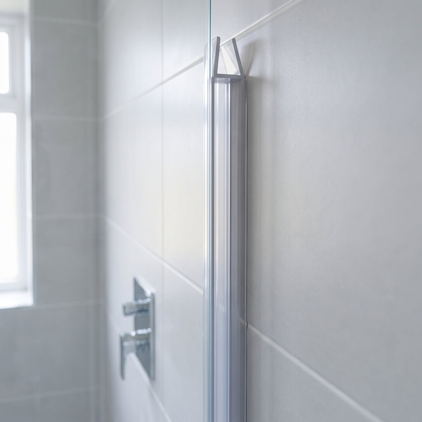 Clear seal fitted down the upright edge of a glass shower screen against a grey tiled wall