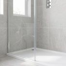 Grey stone-tiled shower recess, chrome-edged glass screen on a white tray, thermostatic valve and window