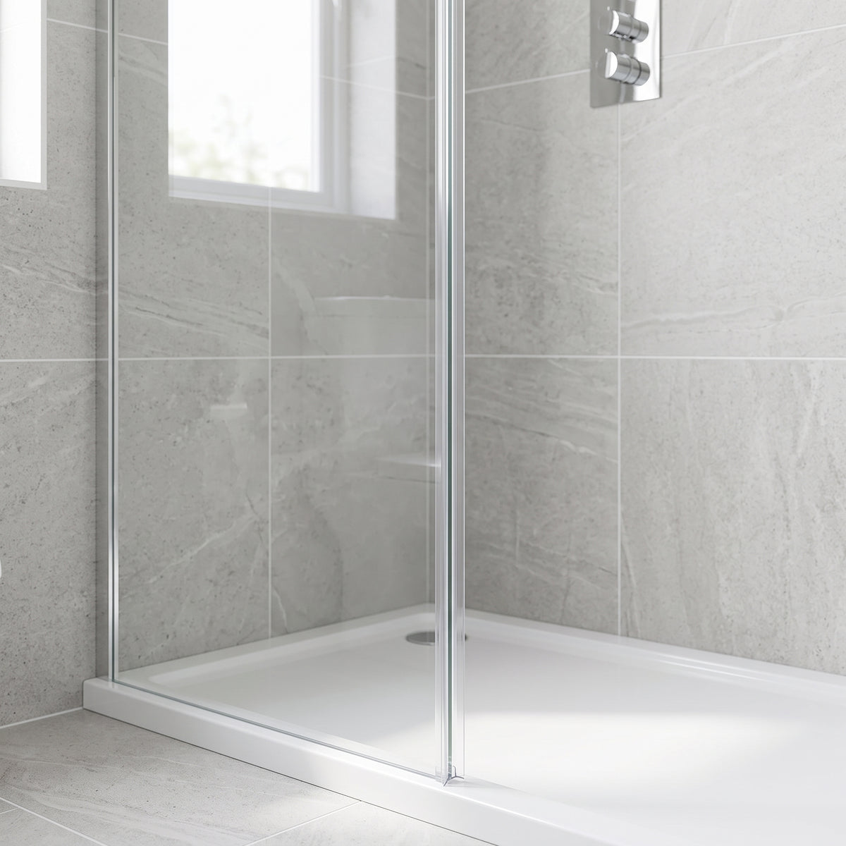 Grey stone-tiled shower recess, chrome-edged glass screen on a white tray, thermostatic valve and window