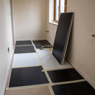 Black and white fluted polypropylene sheets taped down over a carpeted hallway during building work, one black sheet propped by the window