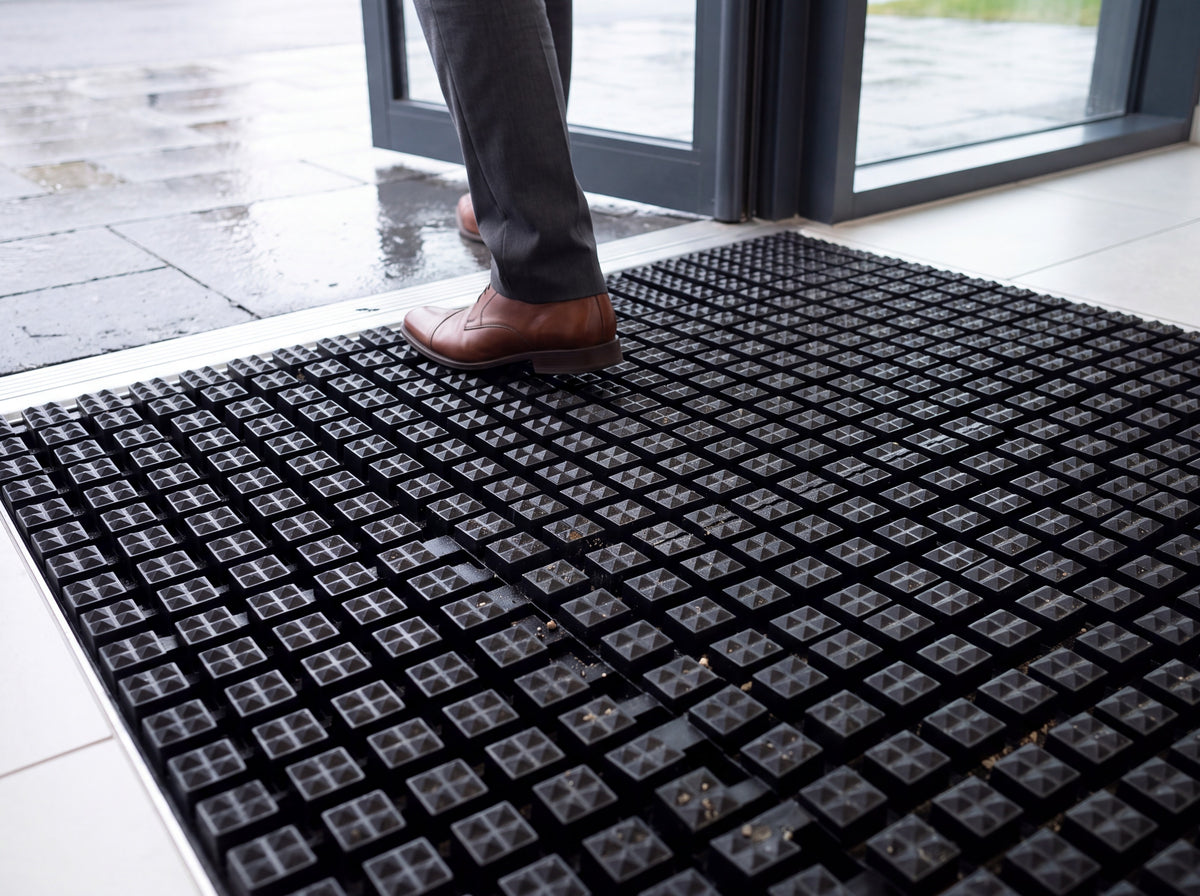 Black open-grid entrance matting recessed in a matwell at a glazed commercial doorway