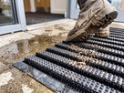 Brush grade entrance matting with nylon bristle strips between the studded bars, a muddy boot scraping across it
