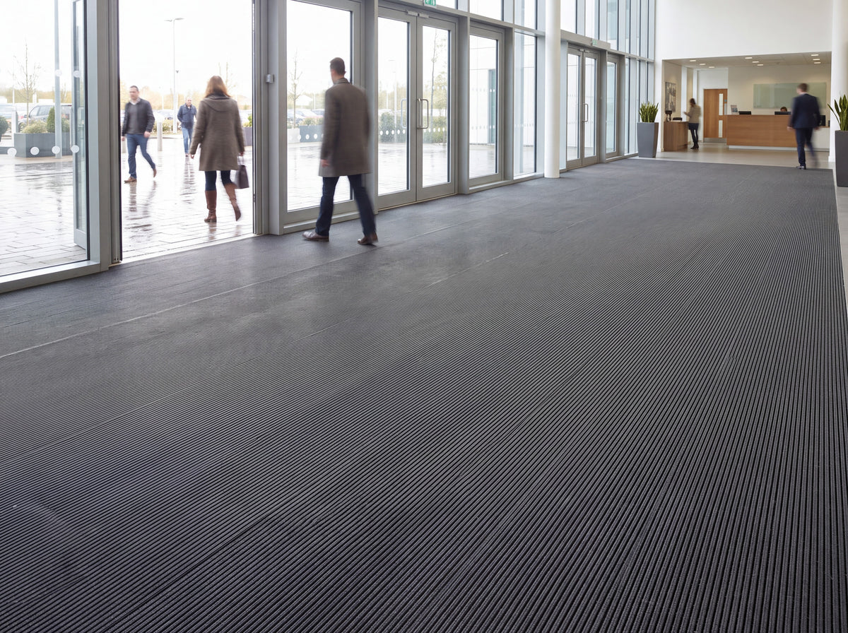 Open-grid entrance matting laid wall to wall across a busy commercial building entrance