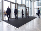 Black Frontrunner Entry 14mm open-grid entrance matting recessed in an aluminium matwell across a corporate office entrance on a rainy morning