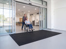Wheelchair crossing flush-laid open-grid entrance matting at a hospital main entrance